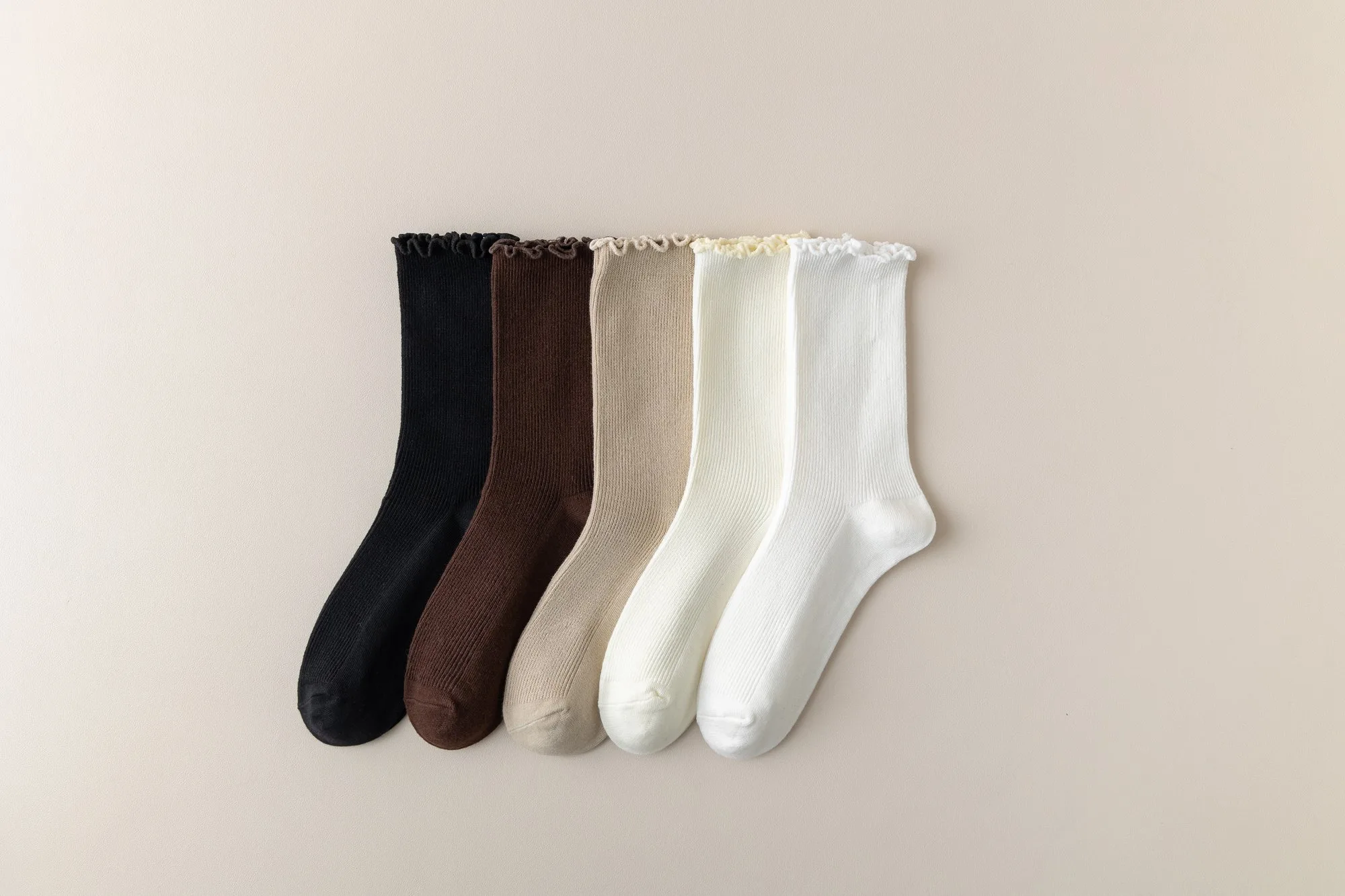 Five pairs of ruffle-edge slouch crew socks laid flat in black, coffee brown, ecru, bleached white and white.
