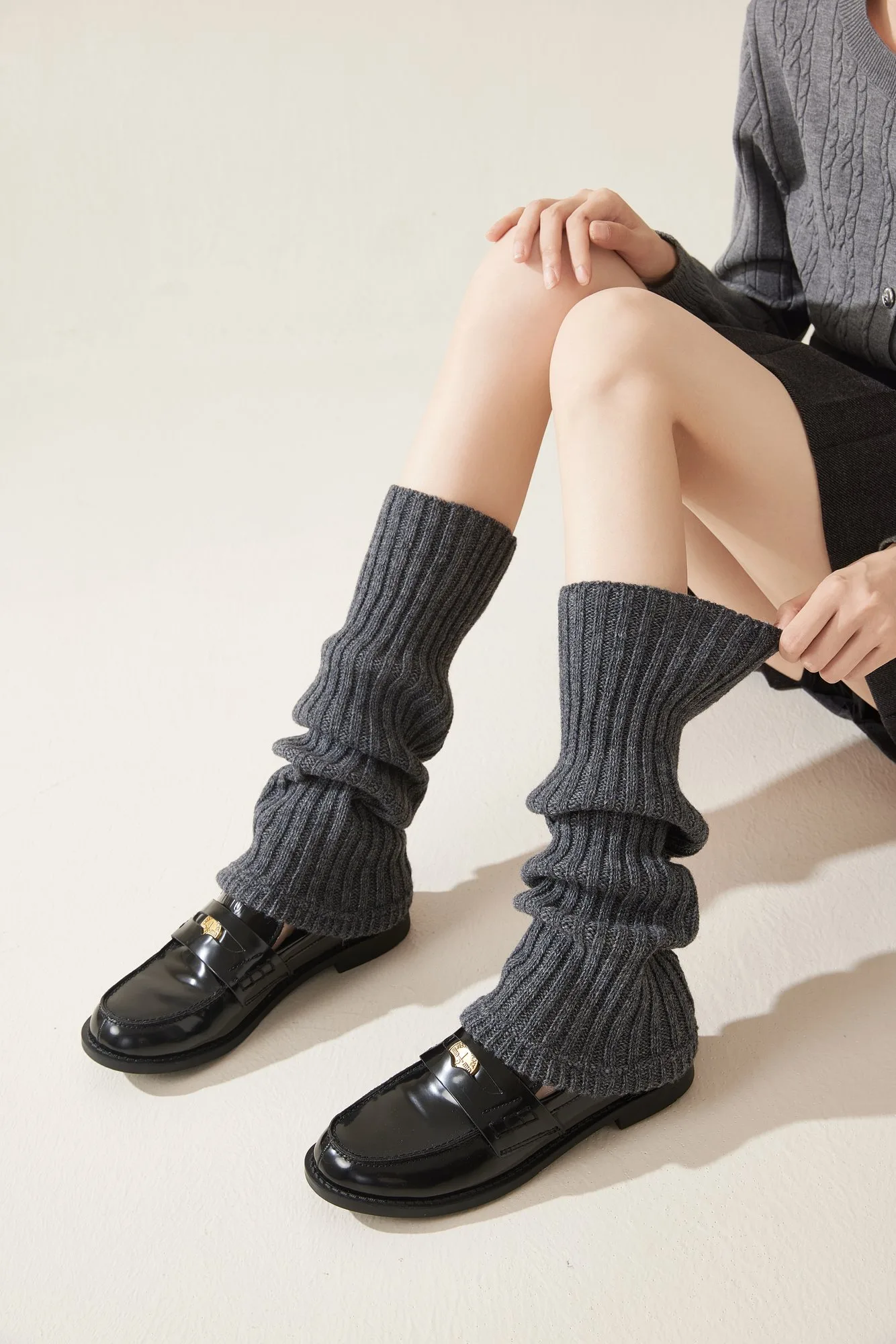 Ribbed slouch leg warmers worn on both legs while seated, showing the rib knit and stacked folds.
