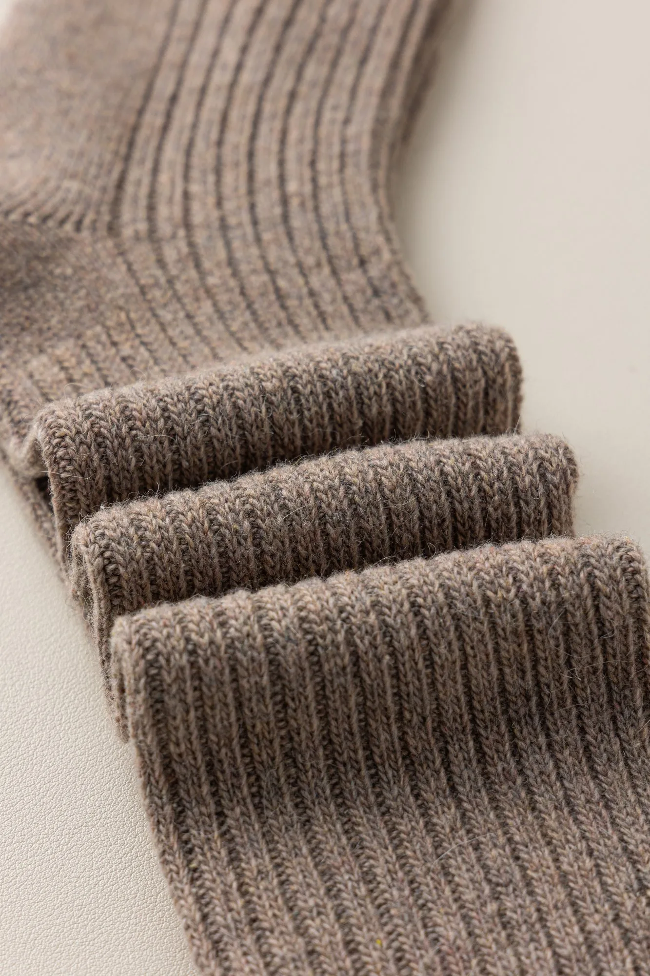 Macro detail of the folded cuff of a wool-blend ribbed knee-high sock, showing the rib and fibre texture.
